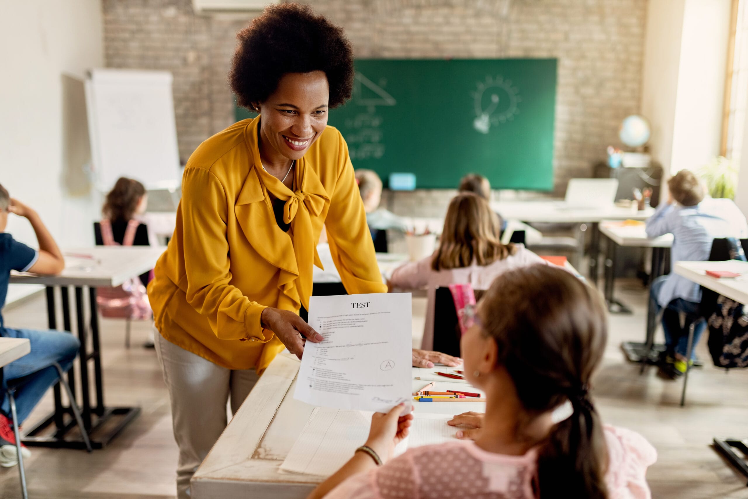 Here are your test results, you got an A! Happy African American teacher giving test results to elementary student in the classroom.